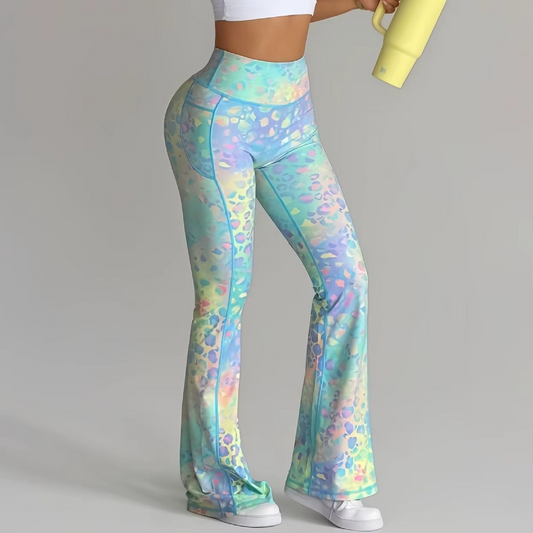 A model wearing high-waisted, flared leggings with a pastel multicolor floral pattern in shades of blue, green, yellow, and purple, holding a yellow mug against a solid gray background.