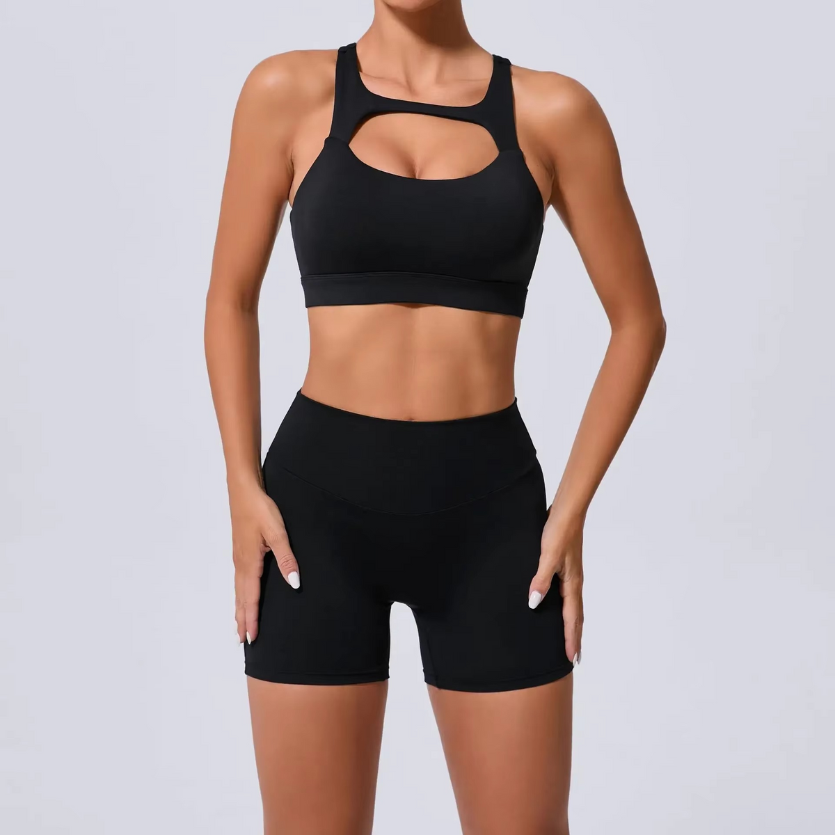 A woman modeling a black sports bra and matching high-waisted shorts against a light gray studio background.