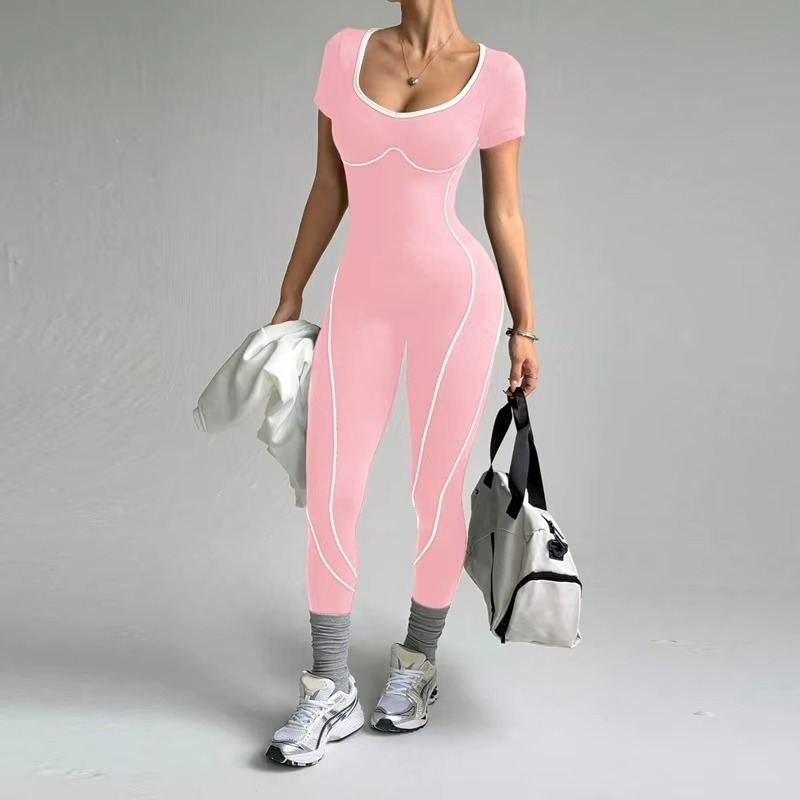 A woman modeling a pink short-sleeve bodysuit with white piping details, holding a white jacket and a gray duffel bag against a plain gray studio background.